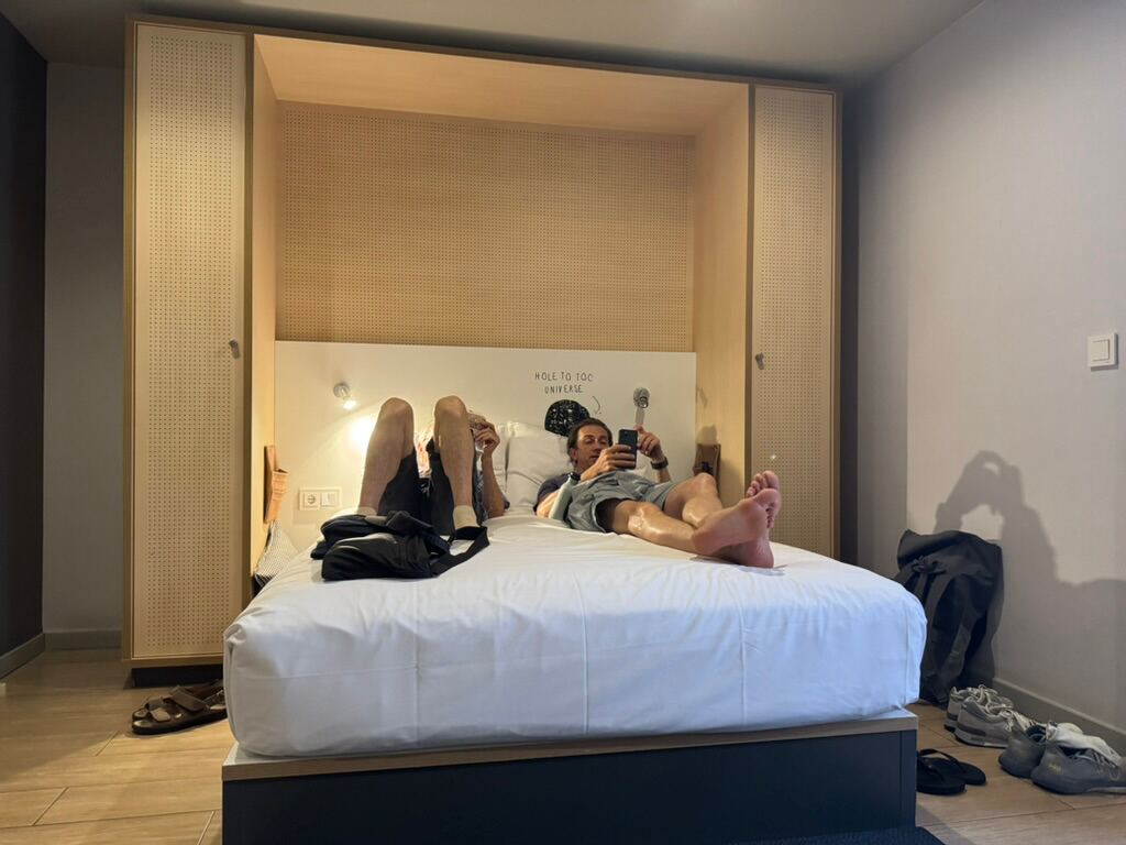 Drei Paar Beine auf dem Bett im Hotelzimmer, Schuhe daneben auf dem Boden